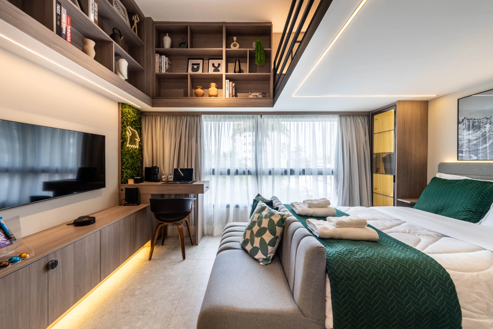 Studio mobiliado com marcenaria planejada, iluminação indireta e enxoval verde